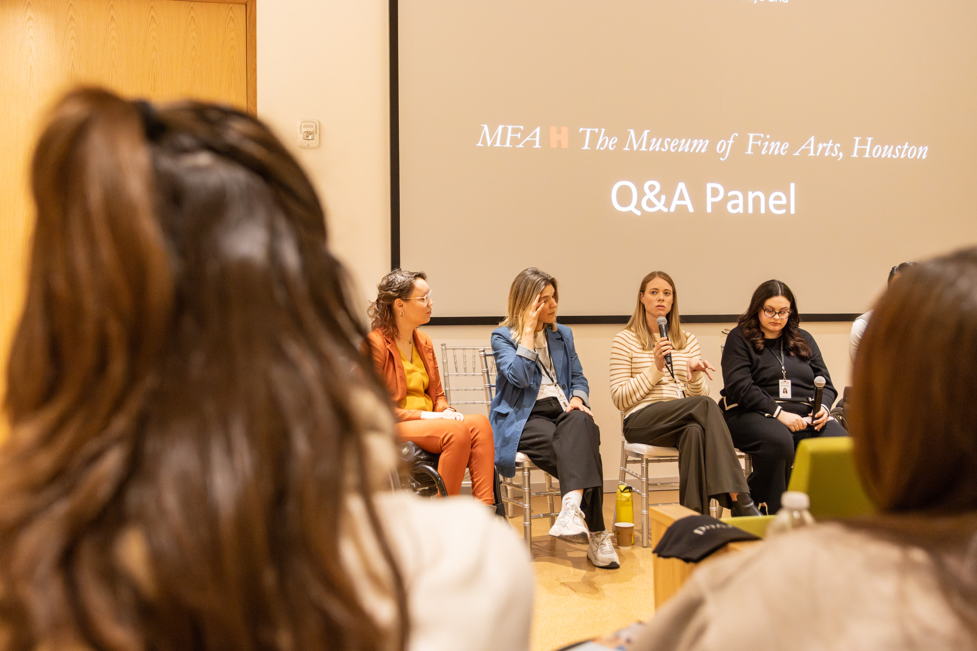 photos by Jens Van Hecke; insta @Jensvh_photos; jensvanhecke@hotmail.com Foto door Jens Van Hecke: op de voorgrond vaag twee achterhoofden, daar tussendoor is een deel van het panel te zien bij het symposium. Op de achtergrond een donker scherm met daarop het logo van het Museum of Fine Arts Houston en de tekst "Q&A Panel".
